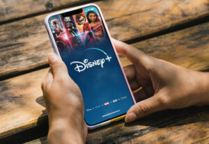 Girl in the park holding a smartphone with Disney+ (Disney Plus) app on the screen. Rustic wooden table. Rio de Janeiro, RJ, Brazil. January 2022.
